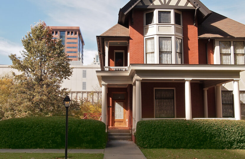 Historic brick house with modern city buildings in the background.