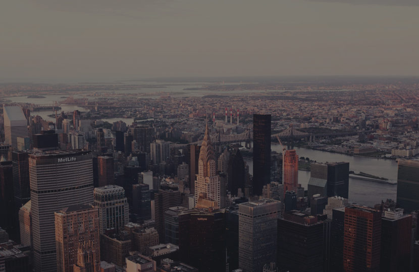Aerial view of a city skyline during sunset with tall buildings and a hazy horizon.